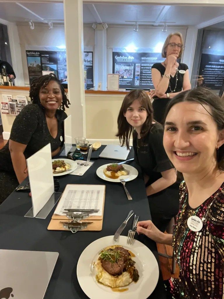 Four people seated at a table in a restaurant, smiling with plates of food in front of them.