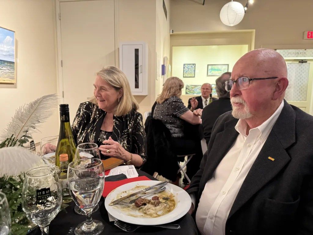 Dinner conversation at a formal event, with wine, plates, and guests seated at a table.