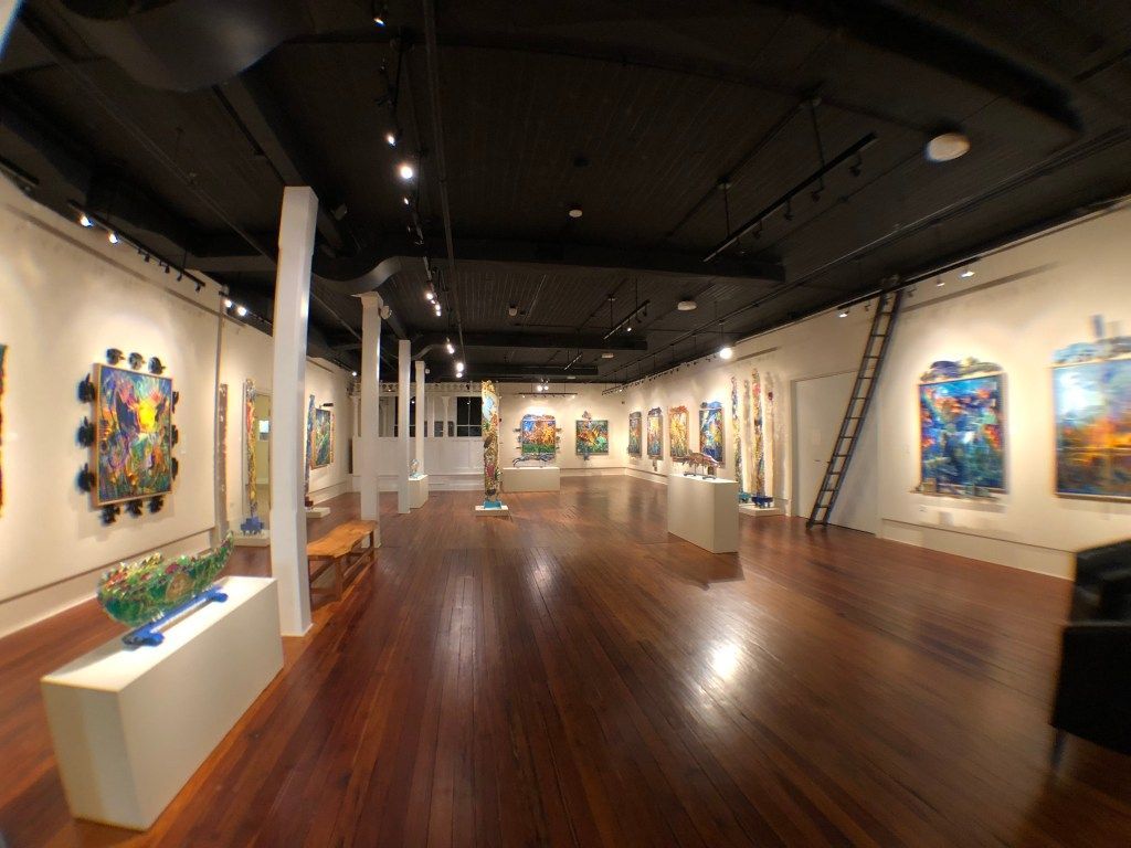 Art gallery interior with colorful paintings on white walls and polished wooden floors.