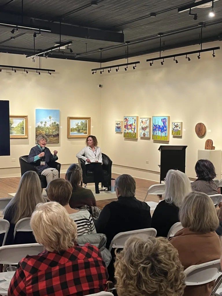 Audience watching a panel discussion in an art gallery with paintings on the walls