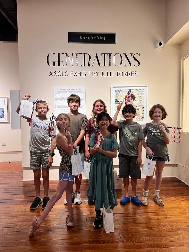 Seven people posing in a museum gallery under a “Generations” exhibit sign