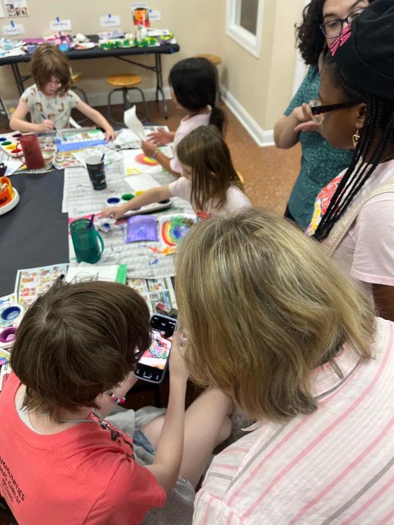 Children doing a group art activity around a table with paints, paper, and supplies