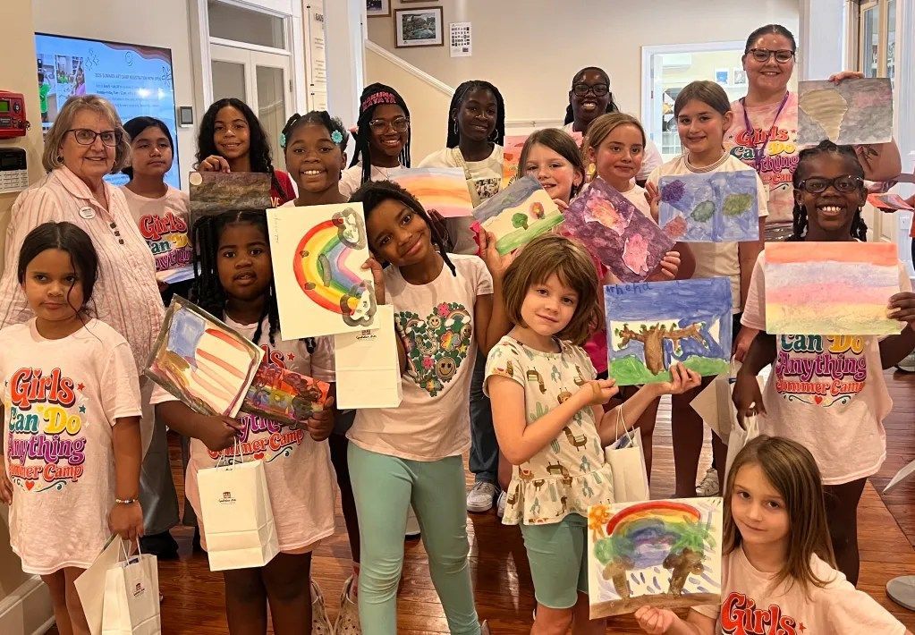 Children hold colorful paintings in a classroom art display.
