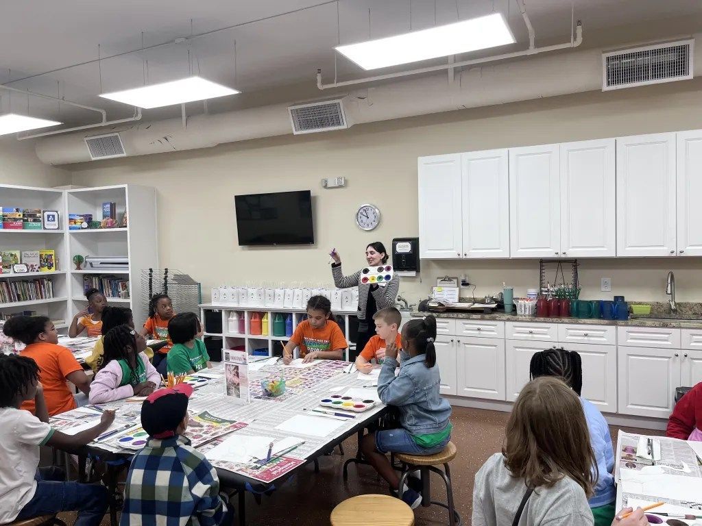 Children seated around tables in a classroom, working on a group craft activity.