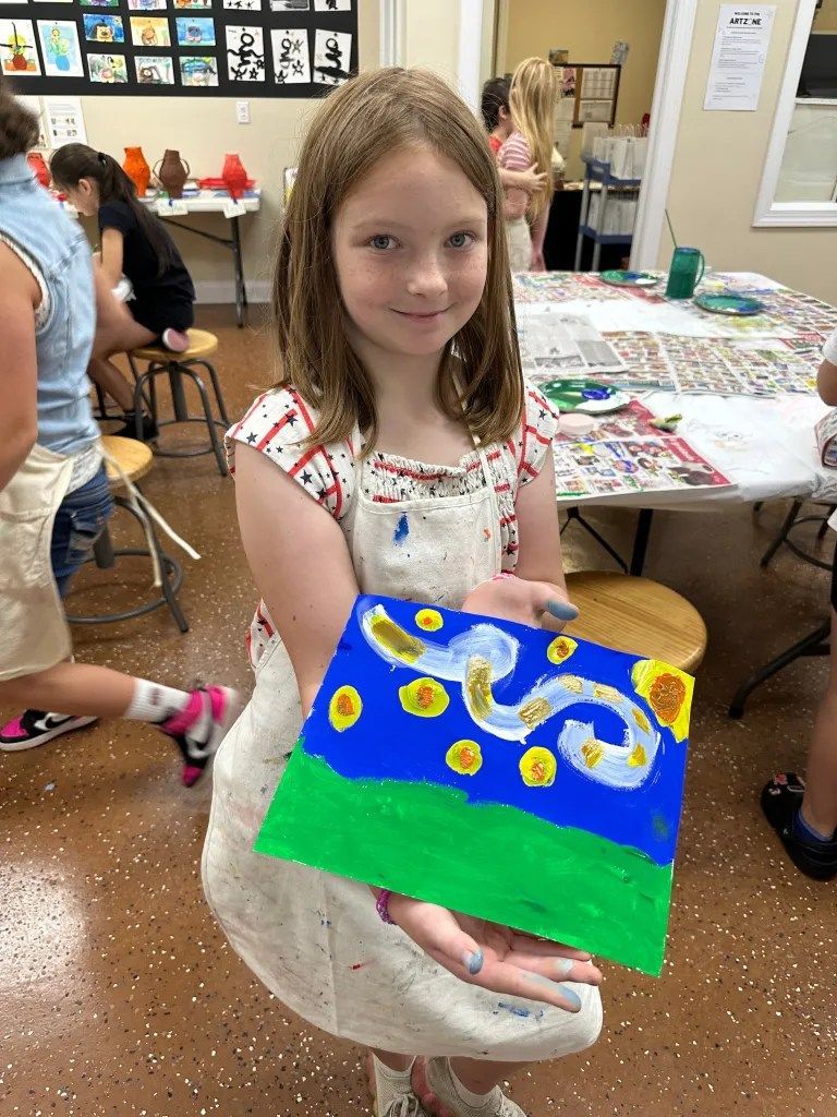 Girl holding a colorful painting with yellow swirls in an art classroom