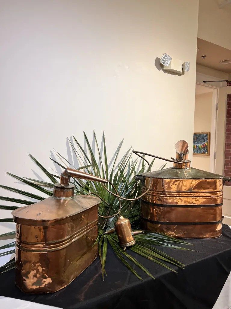Copper containers with lids on a black table, decorated with green palm fronds and gold accents.