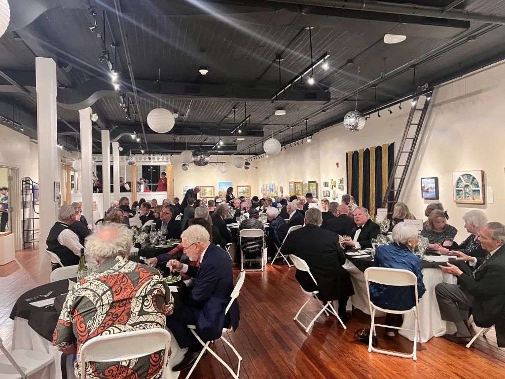 Crowded restaurant dining room with people seated at tables under pendant lights and a black ceiling