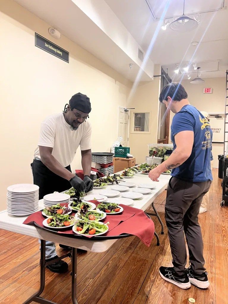 Two people preparing food at a buffet table in a bright room
