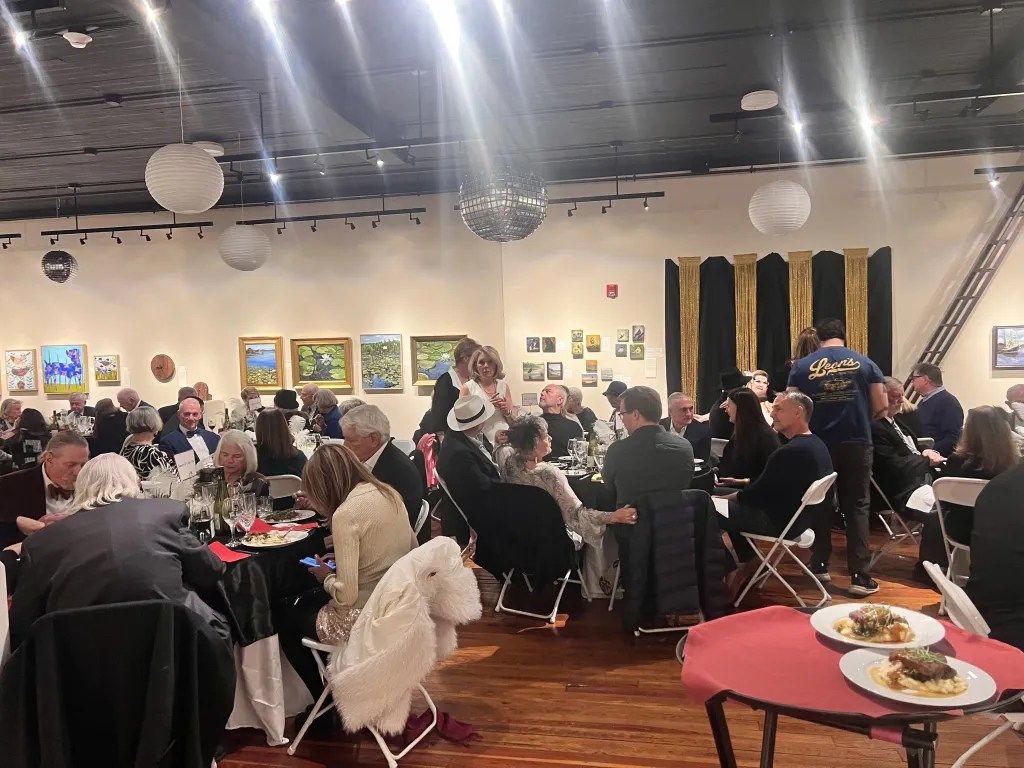 Crowded indoor banquet with people seated at tables, colorful wall art, and hanging paper lanterns