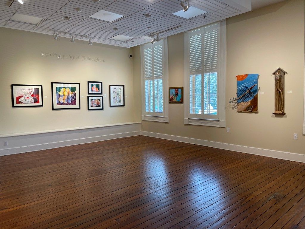 Empty gallery room with framed artwork on white walls and a polished wood floor