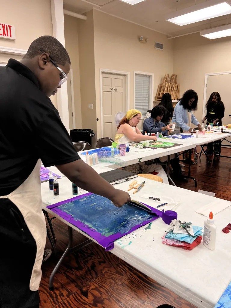 People working at tables painting canvases in an indoor art workshop