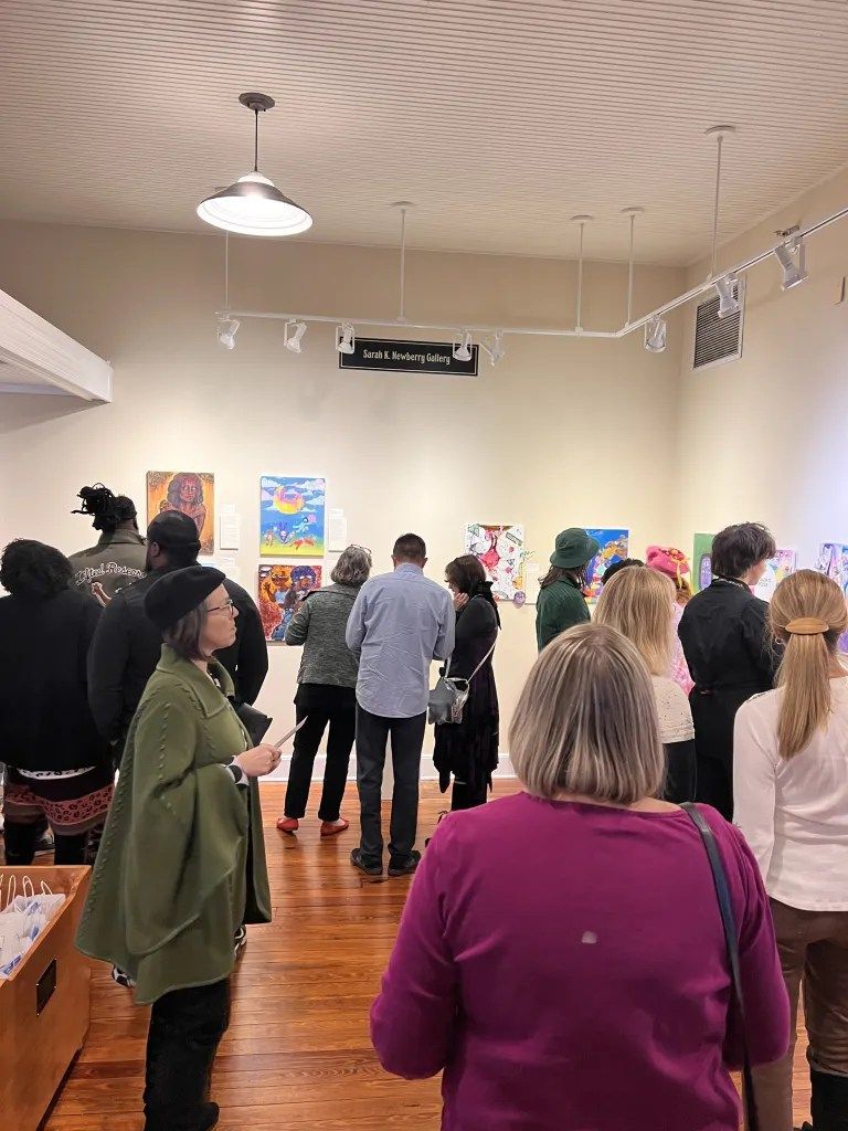 Crowd of people standing in an art gallery, viewing colorful wall displays under bright lights.