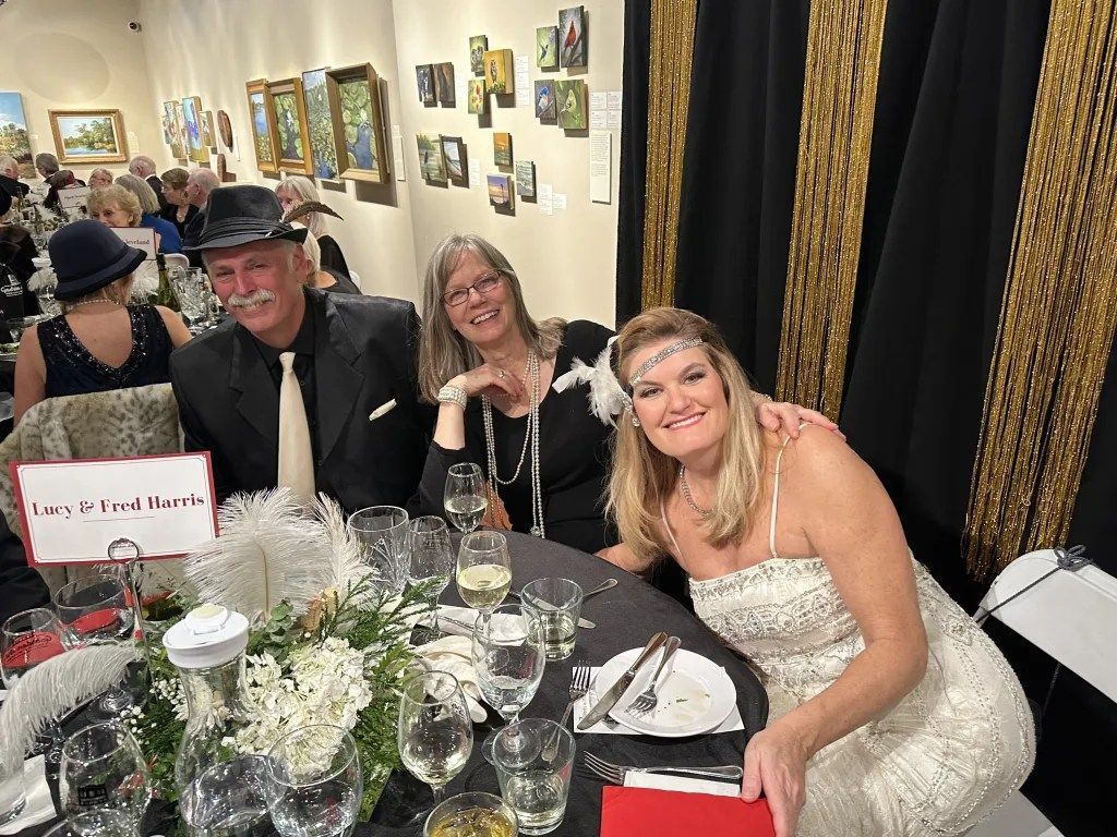 Three people smiling at a decorated dinner table in an art gallery event space