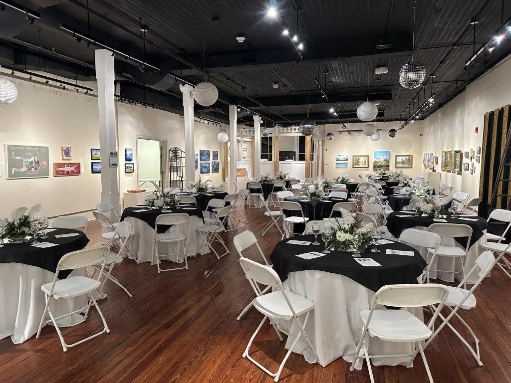 Empty event hall with round tables, white chairs, and framed art on the walls