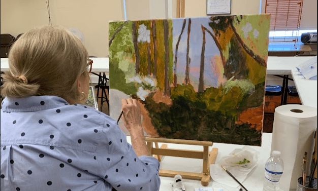 Artist painting a colorful forest landscape on a canvas in a studio