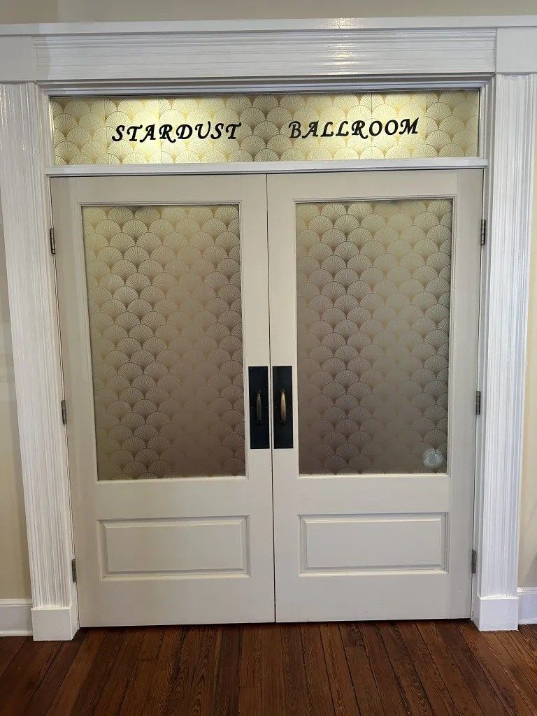 Double white doors with frosted glass panels under a sign reading “Stardust Ballroom”