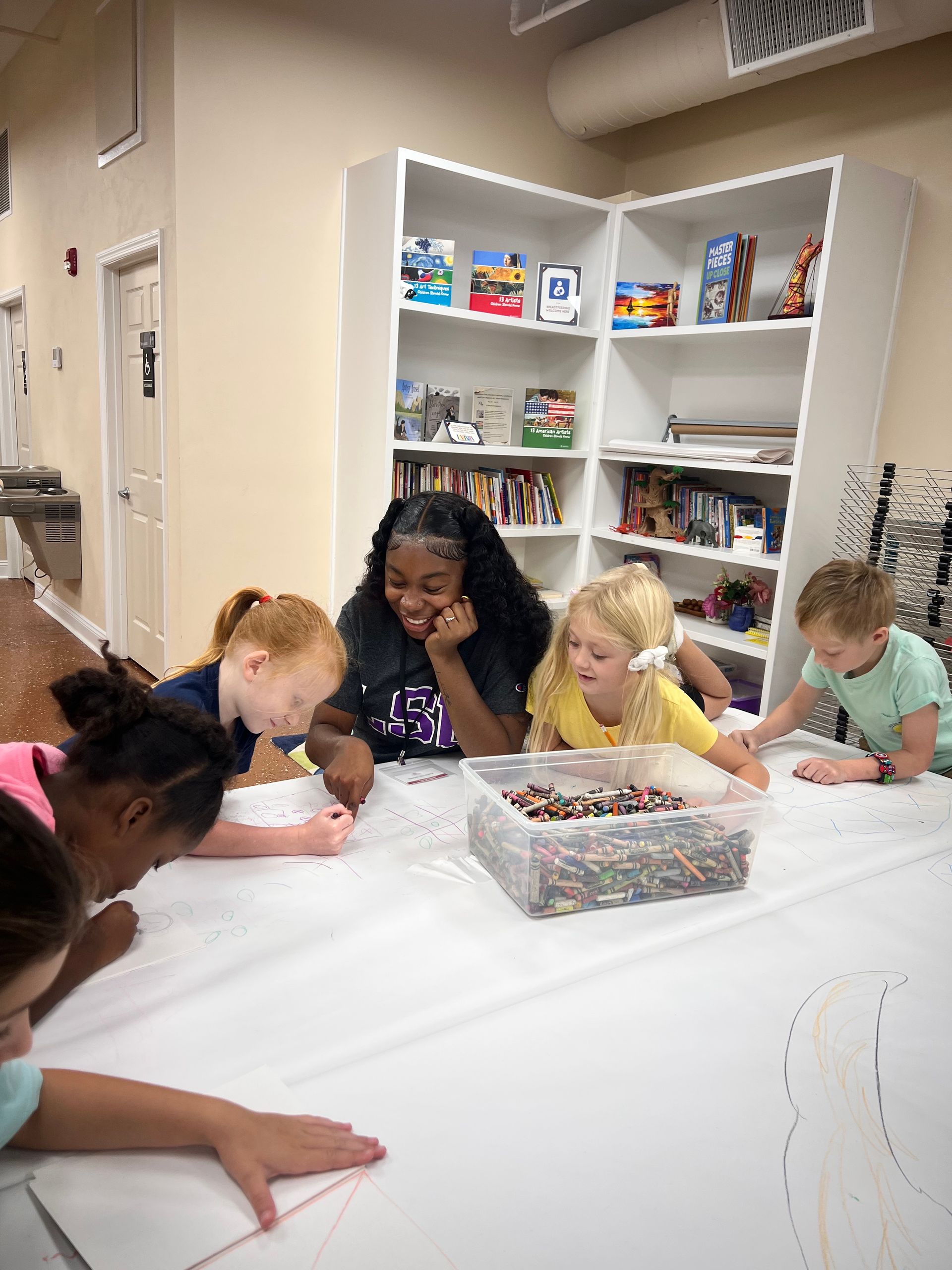 Children leaning over a table, playing with colorful beads in a bright classroom craft area
