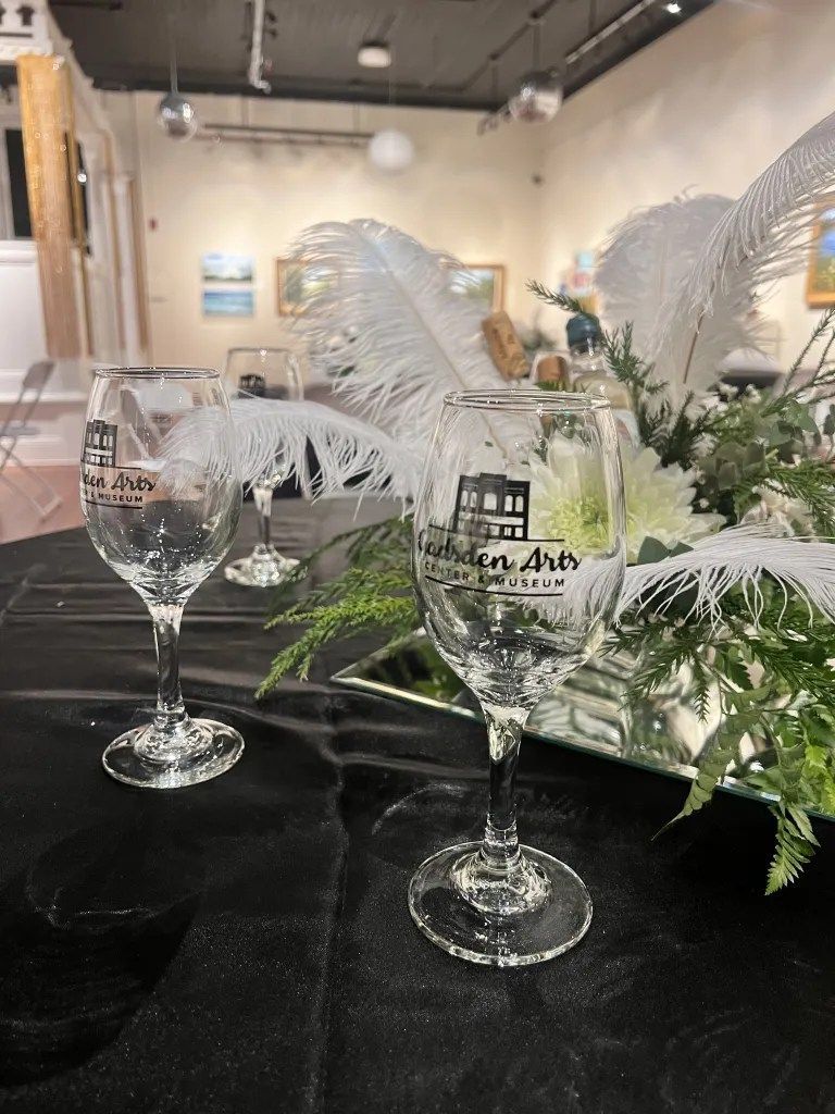 Two clear wine glasses on a black table with white feather floral decor in an elegant indoor venue