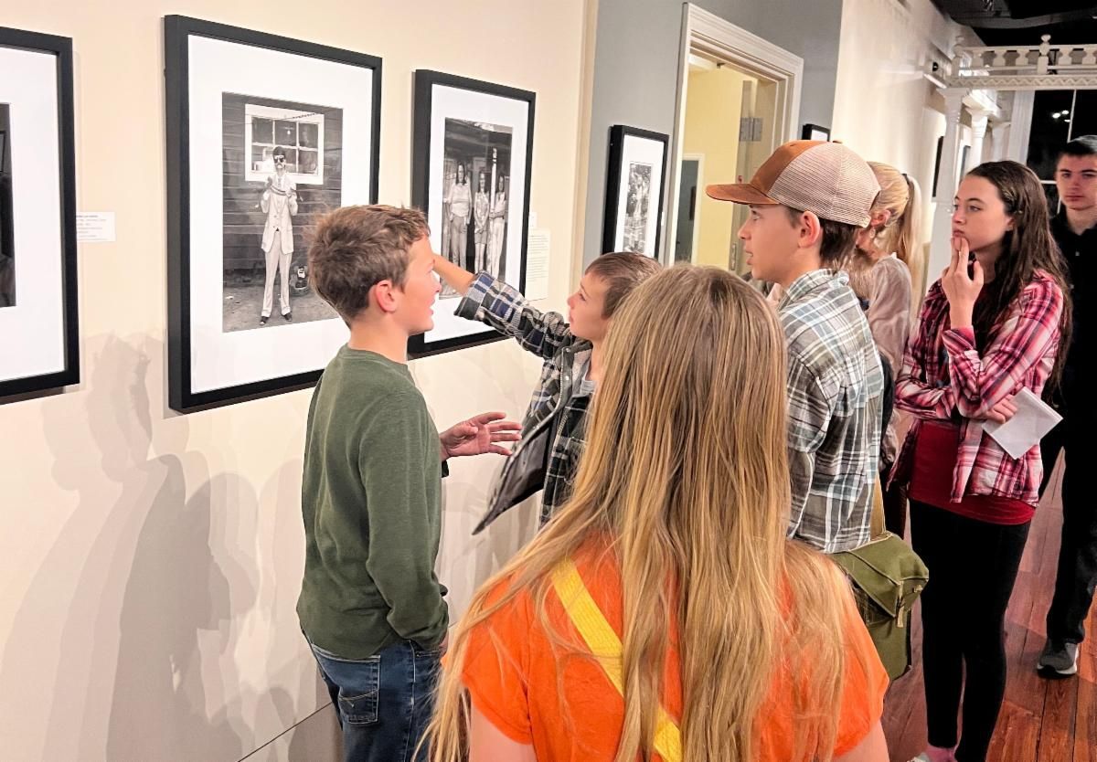 People viewing framed black-and-white photos in a gallery hallway