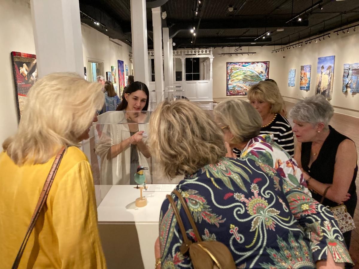 People gathered around a display in a gallery, examining artwork and speaking quietly.