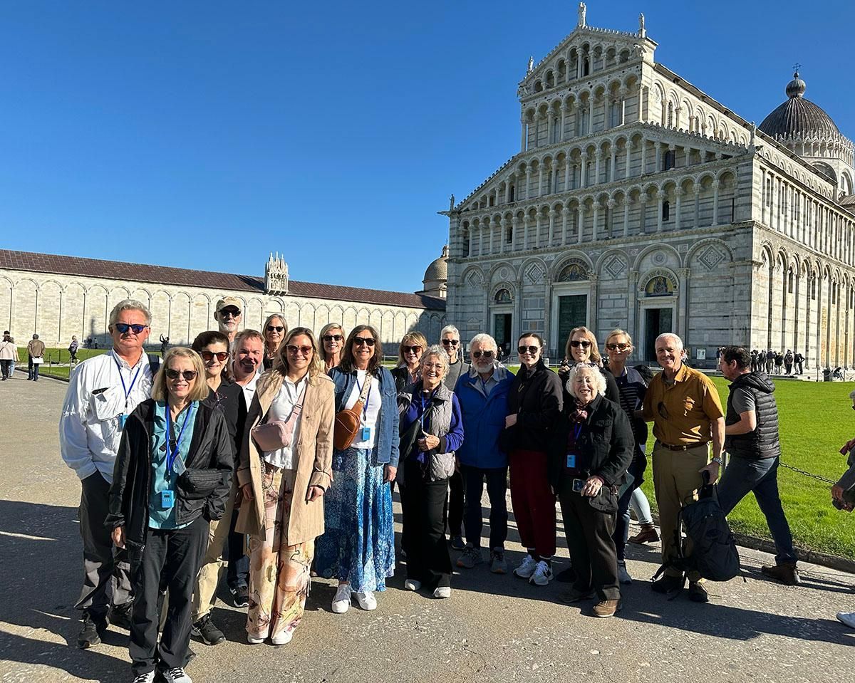 Group of tourists posing outside the ornate Pisa Cathedral on a sunny day