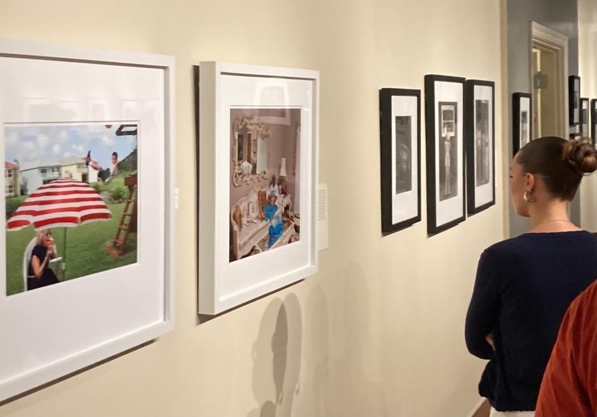 Art gallery hallway with framed photos on a cream wall; a woman stands viewing the exhibit.