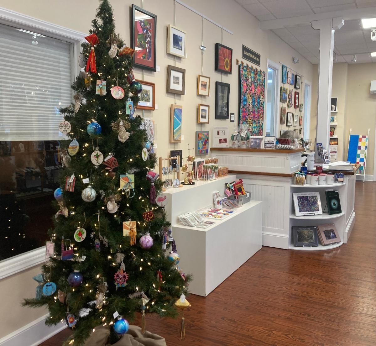 Holiday-decorated office lobby with a lit Christmas tree, framed art walls, and white display shelves
