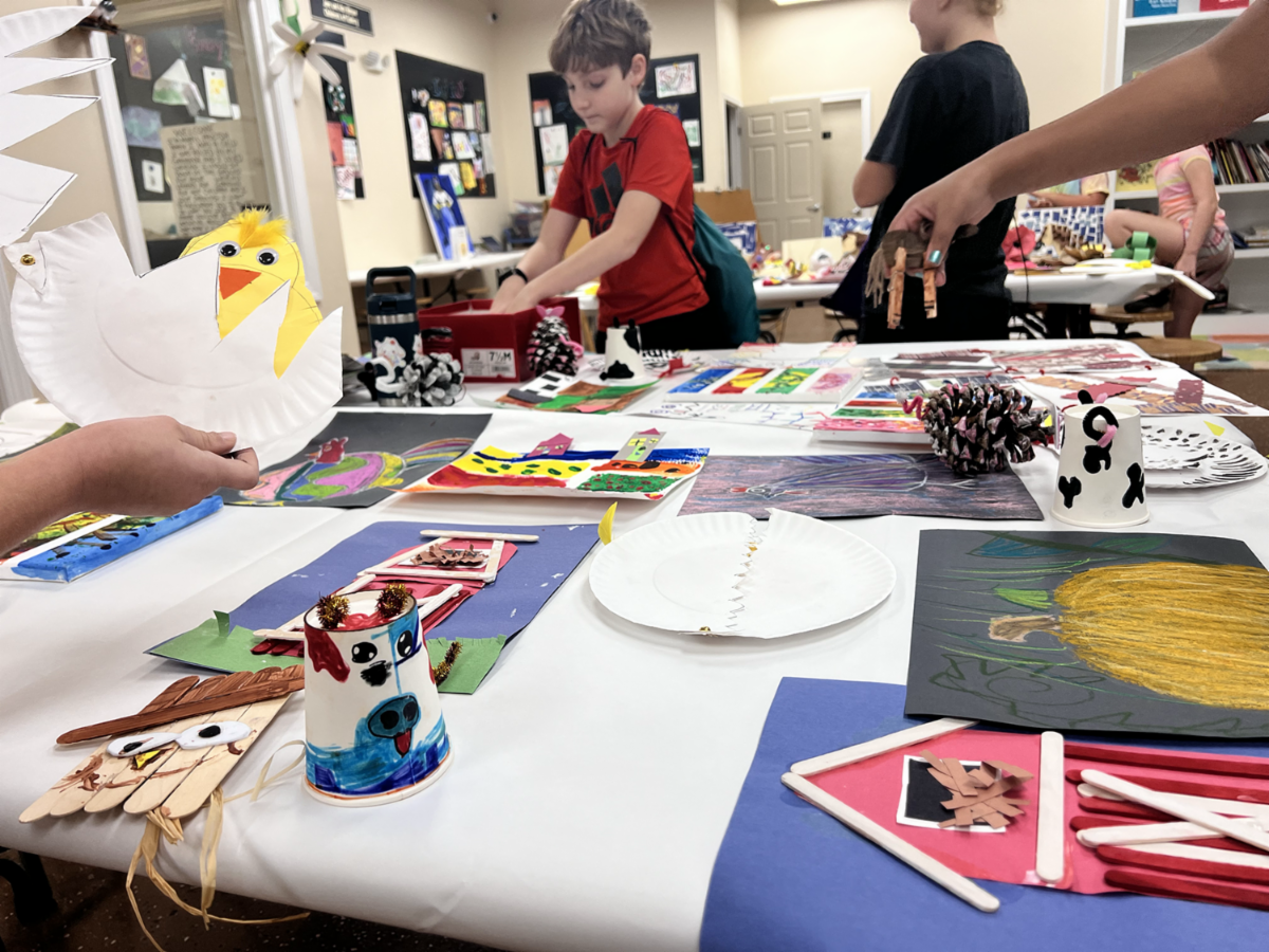 People gathered around a table of colorful craft projects at an indoor workshop.