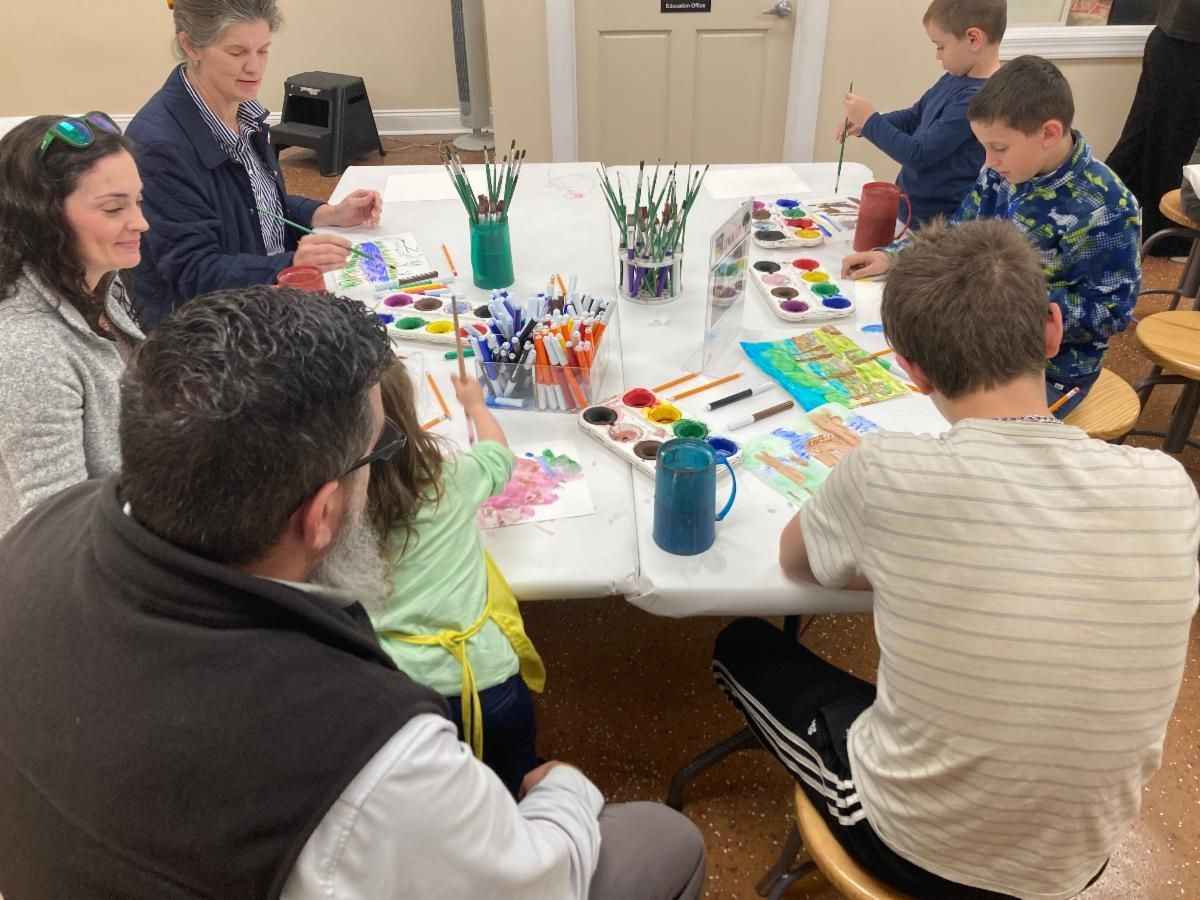 People around a table painting and drawing with art supplies in a bright room