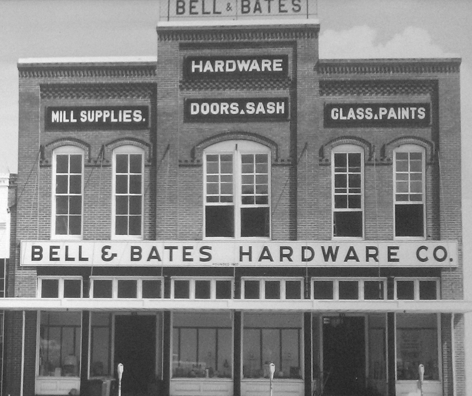 Black-and-white storefront of Bell & Bates Hardware Co. with signs for hardware, doors, sash, and glass paints