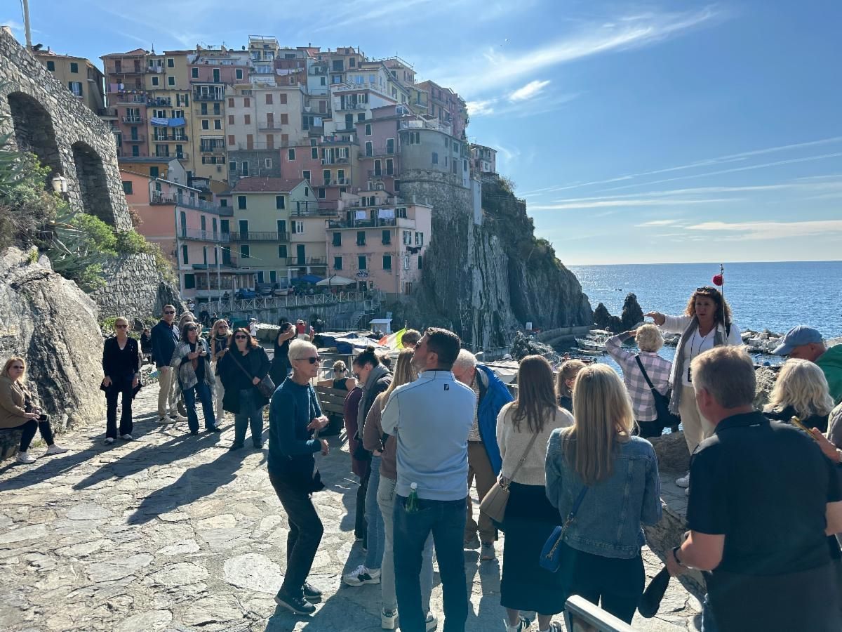 Crowded seaside path beside colorful cliffside buildings under a bright blue sky