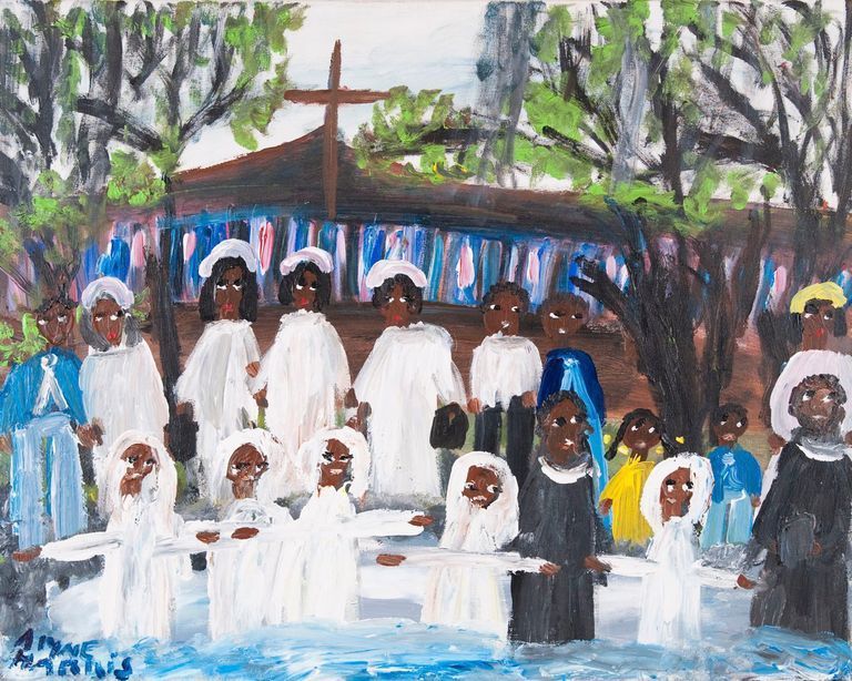 Group in white robes gathered outdoors before a cross and blue-and-white backdrop, with trees and water in front.