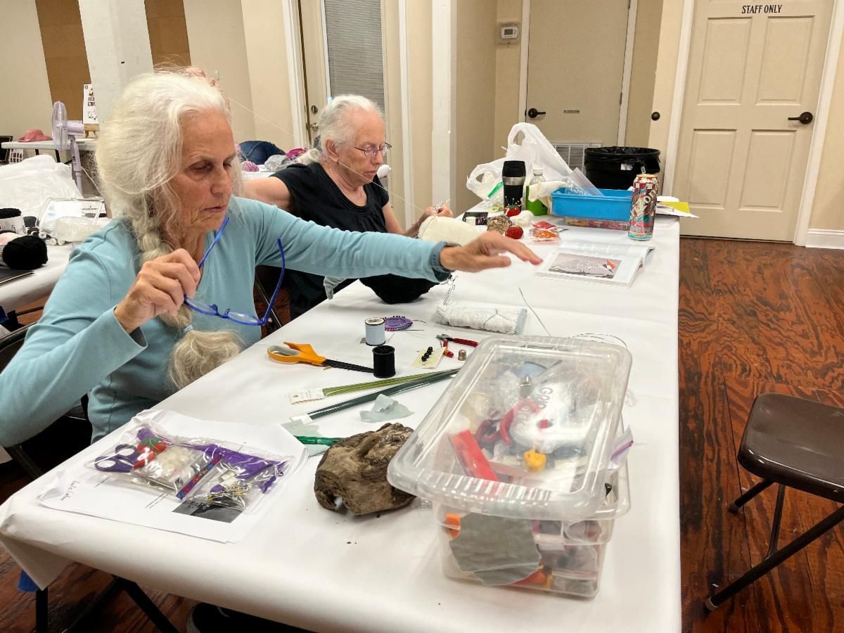 Two people crafting at a table with tools, plastic bins, and supplies in a bright room