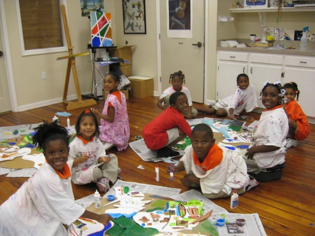 Children sitting on the floor painting and drawing in an art classroom
