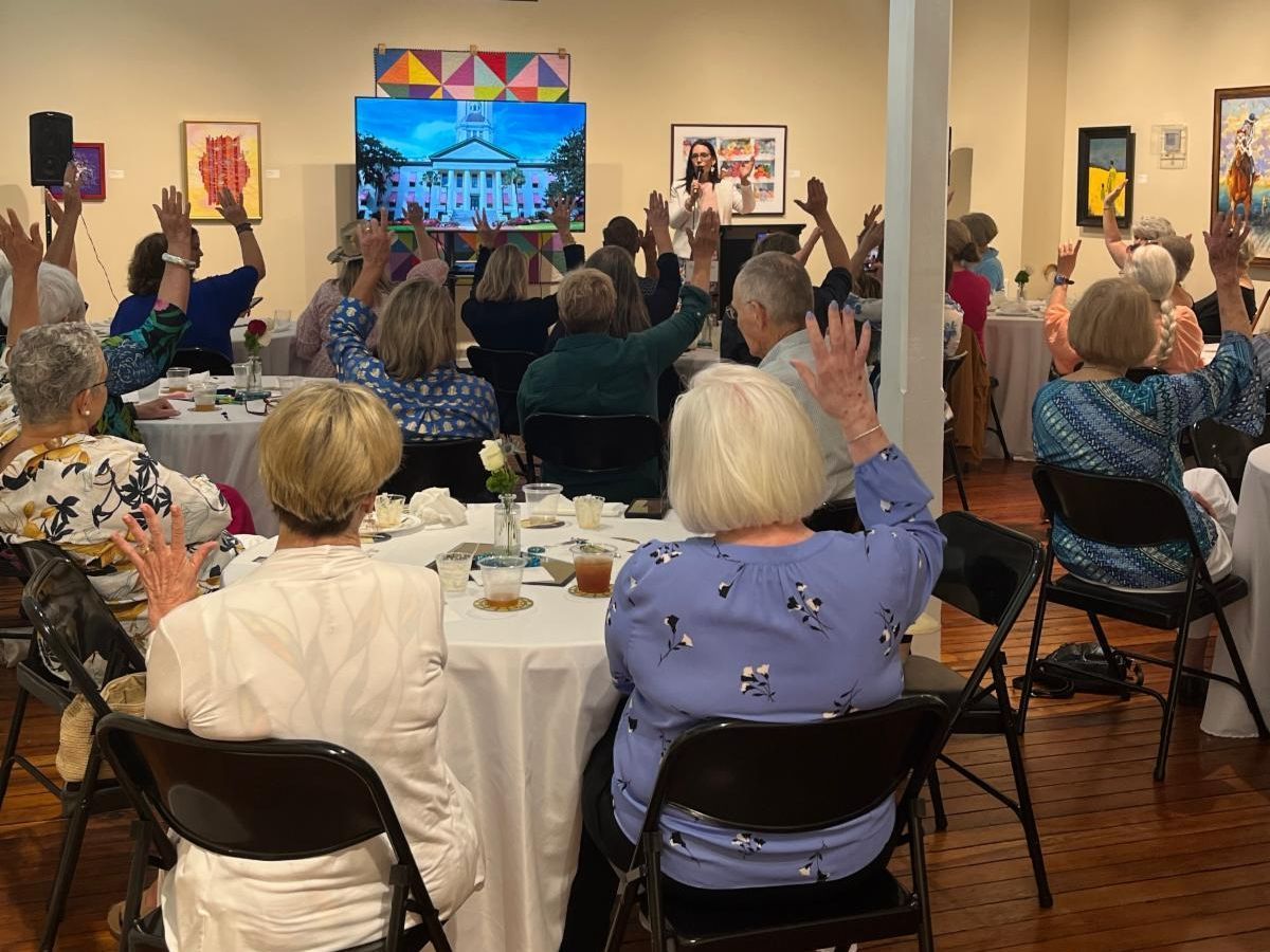 Audience raises hands at a banquet hall event with a colorful stage screen.