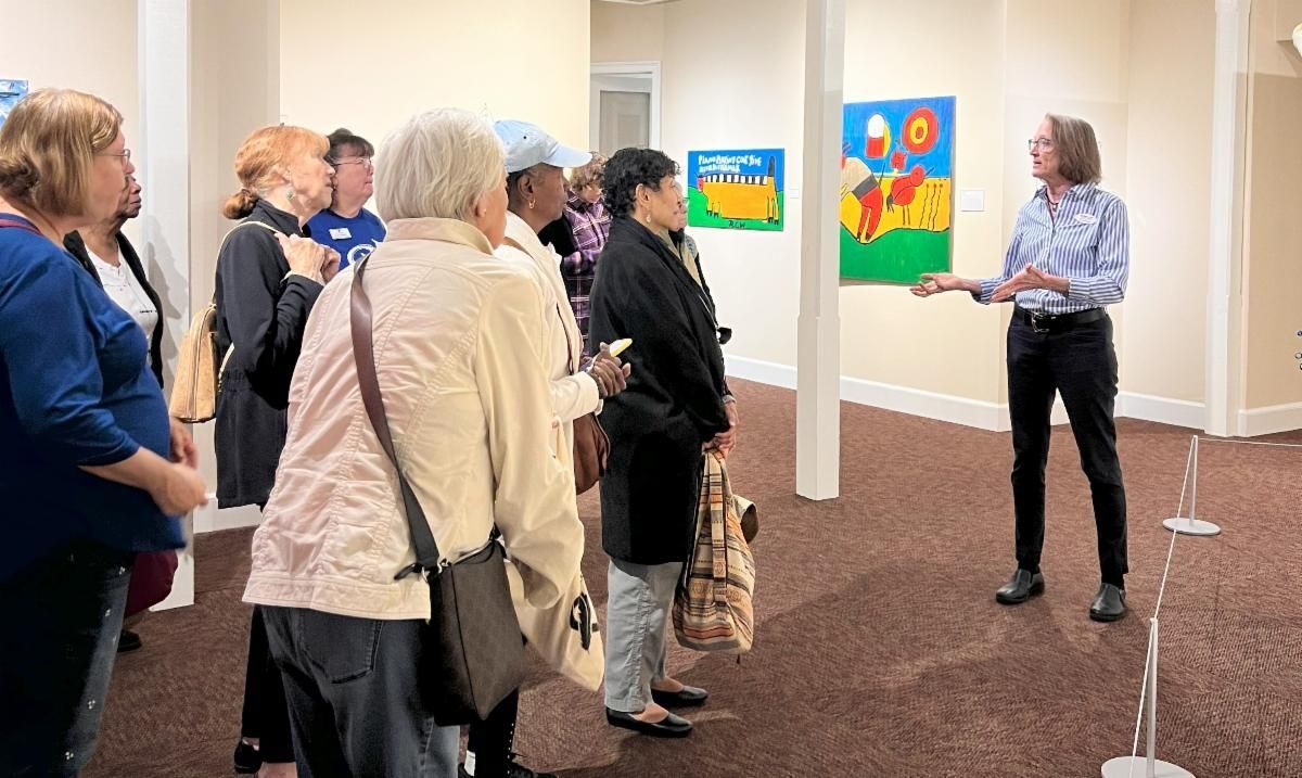 Small group listens to a speaker in an art gallery with colorful paintings on the walls.
