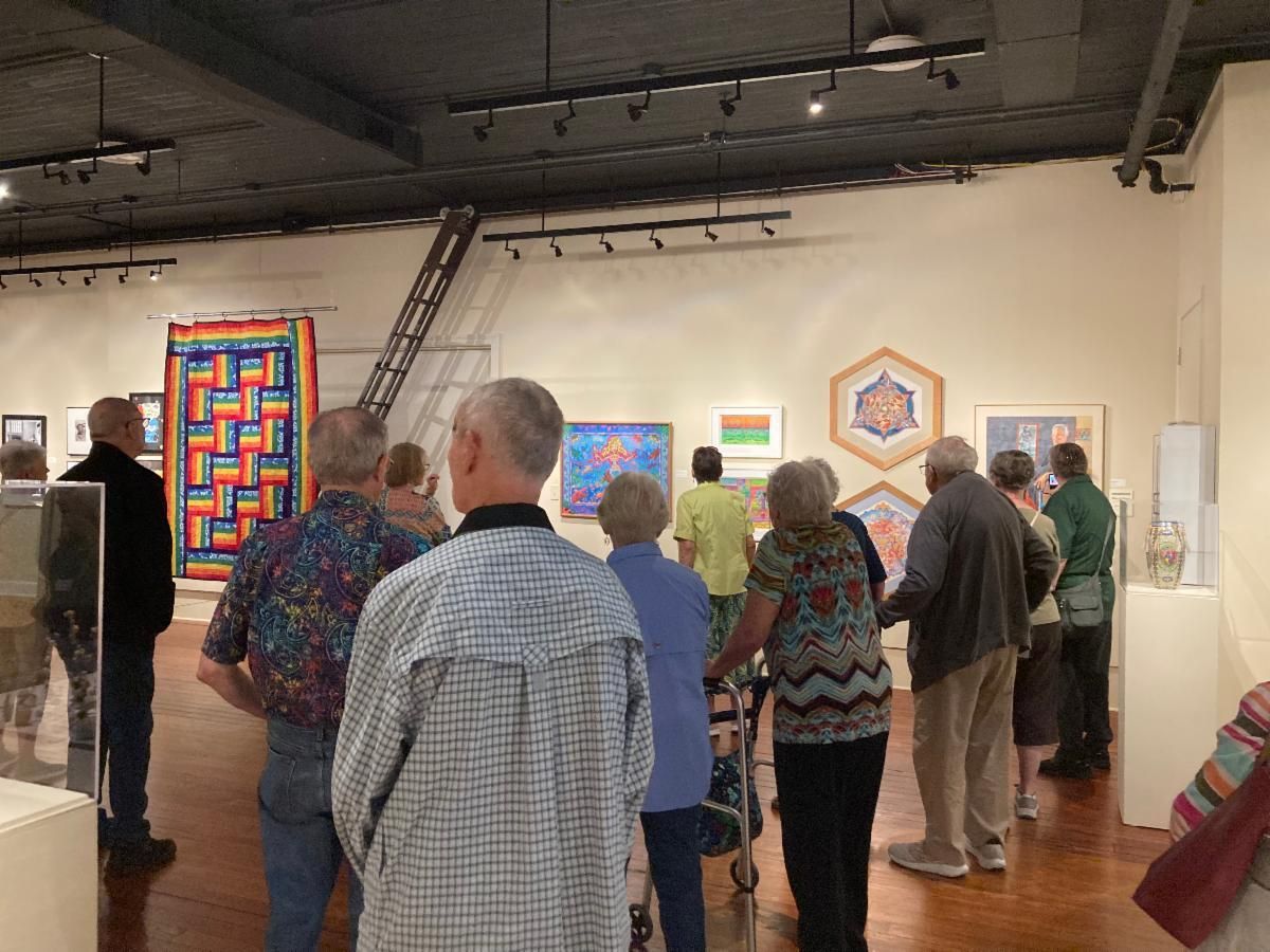 Visitors viewing colorful quilts in an art gallery.