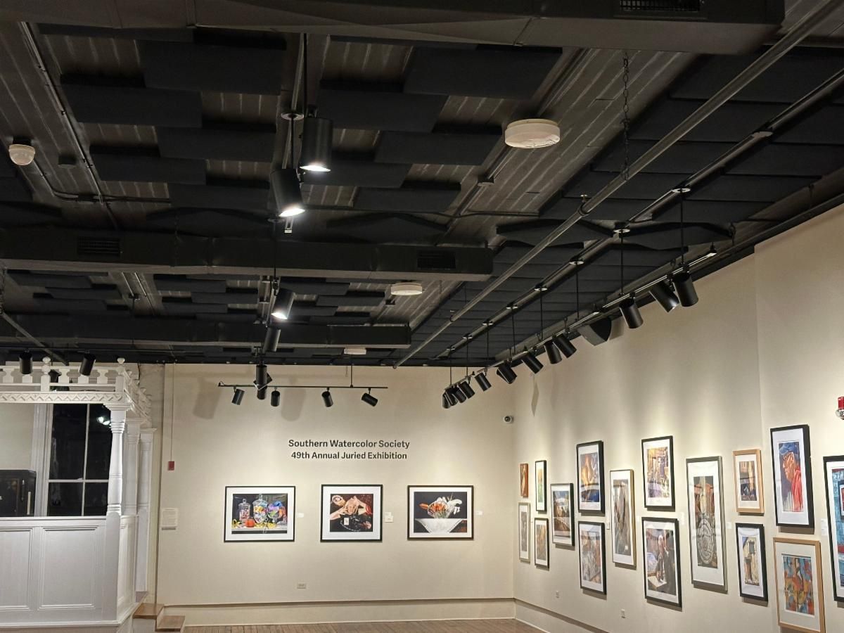 Art gallery wall with framed paintings and photographs under black ceiling track lights