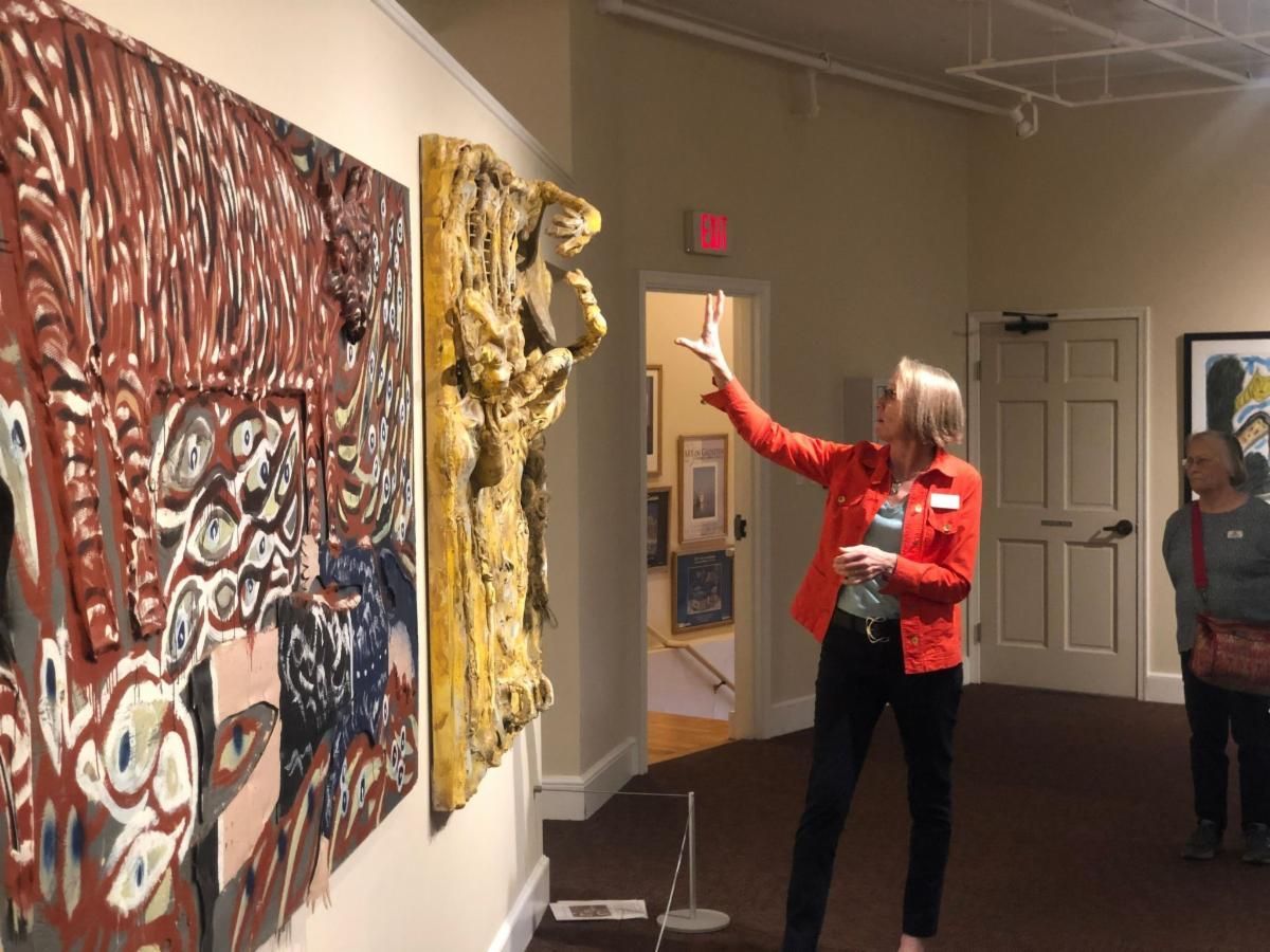 Woman in red jacket pointing at wall art in a gallery, with two large abstract paintings on display
