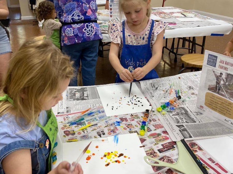 Children painting at a table covered with newspapers and colorful art supplies.