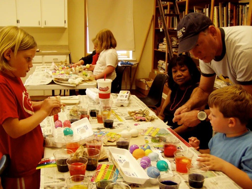 People decorating colorful Easter eggs at a table in a classroom or kitchen setting