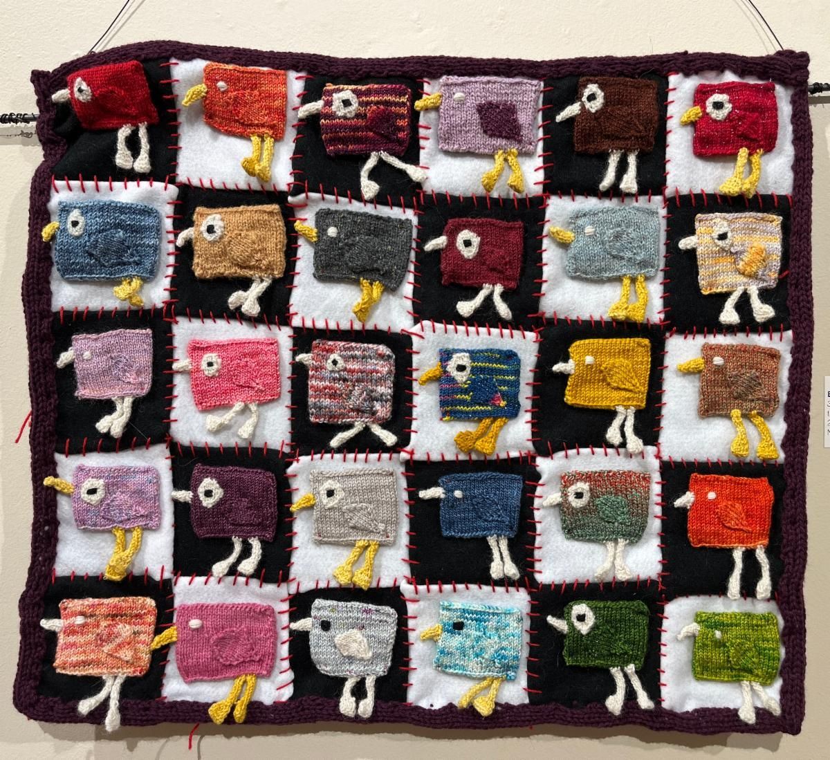 Colorful patchwork fabric with small square faces and yellow ribbon legs on a dark border