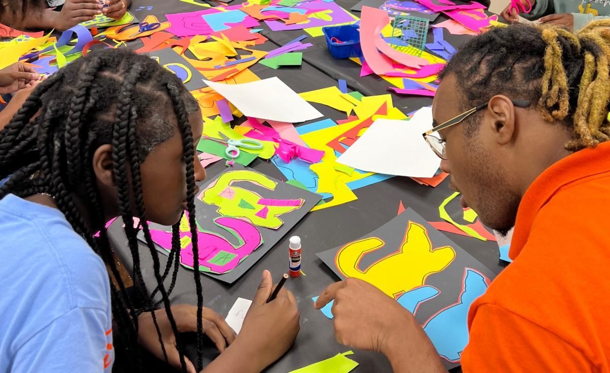 Two people working on a colorful paper collage spread across a table