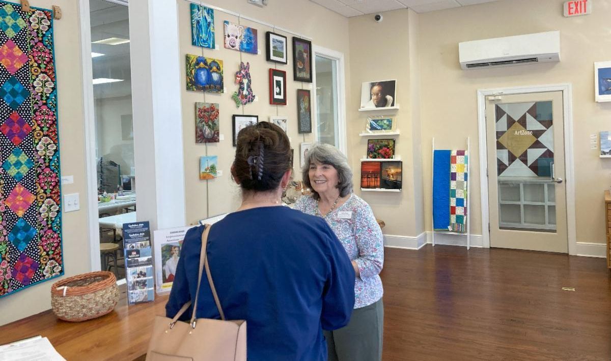 Two people talking in an art gallery with colorful wall displays and wooden floors