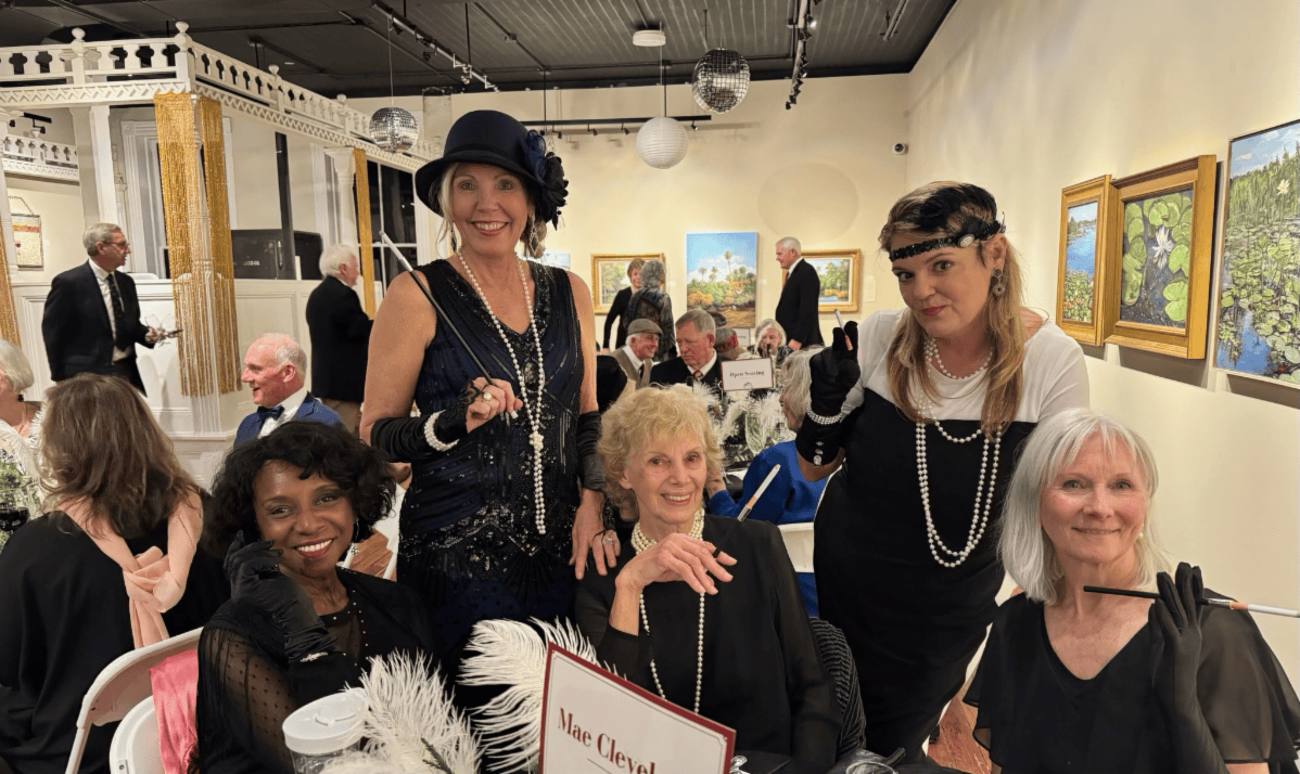 Group posing in an art gallery, with three seated and two standing, all in black clothing and hats.