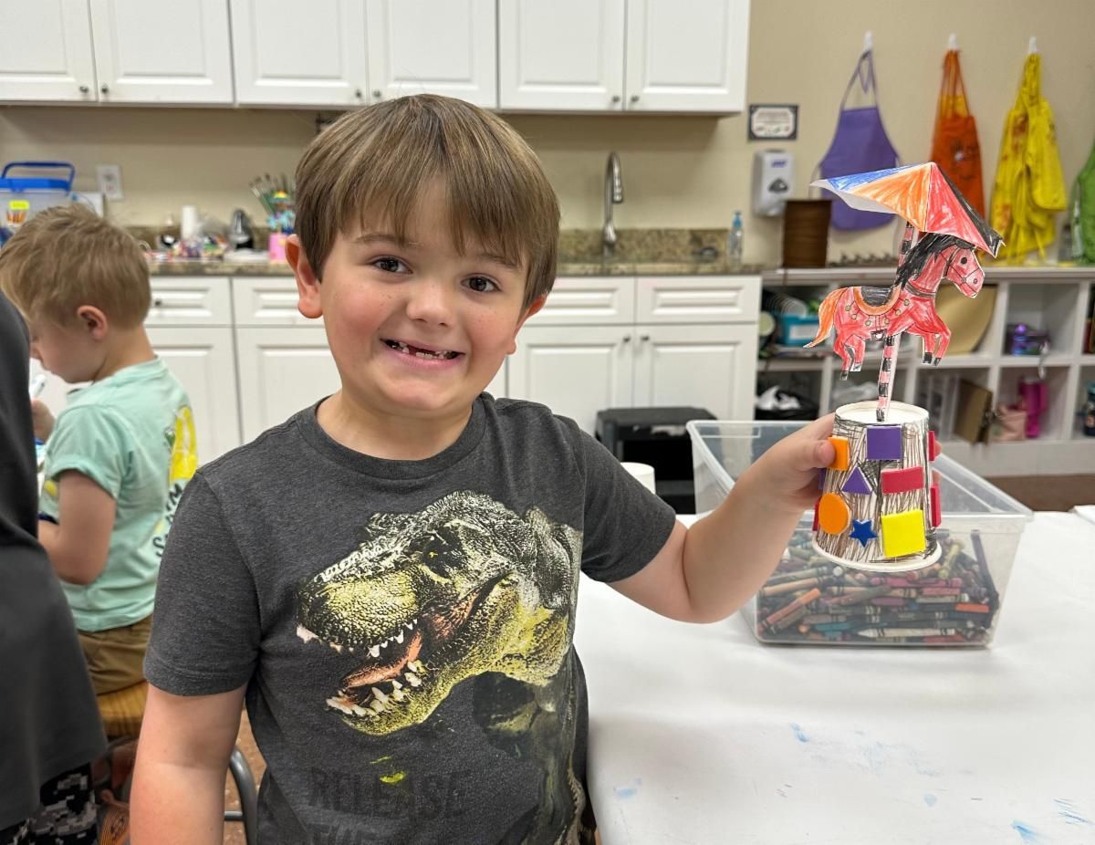 Smiling child in a classroom holding a colorful craft project