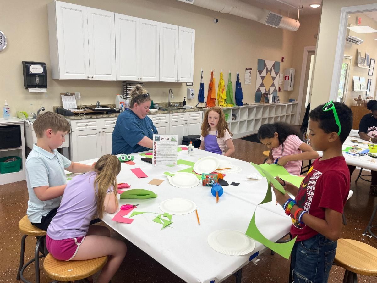 Children crafting at a table with an adult in a classroom, surrounded by colorful paper and supplies