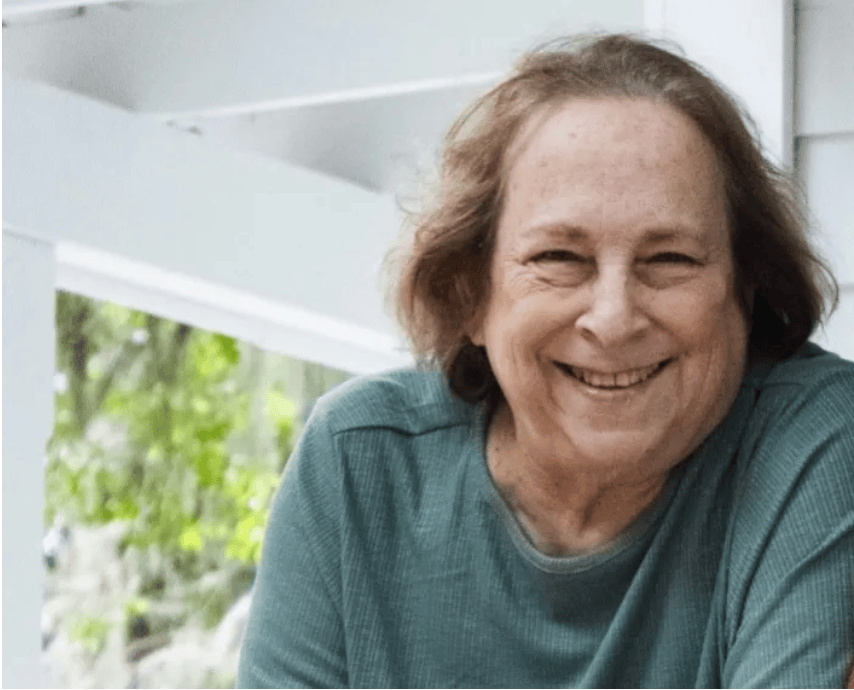 Smiling woman in a teal shirt sitting outdoors on a porch