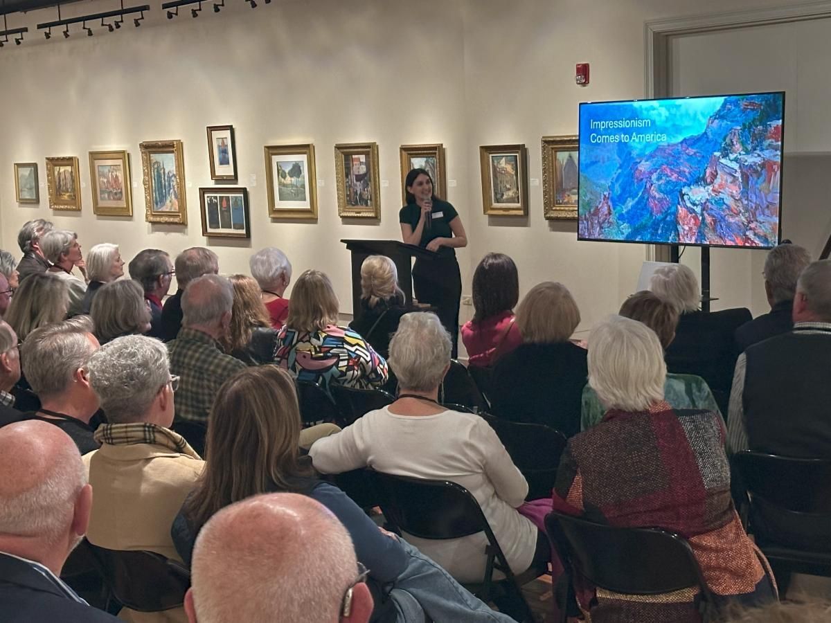 Audience seated in a gallery, watching a presenter beside a screen with a colorful image.