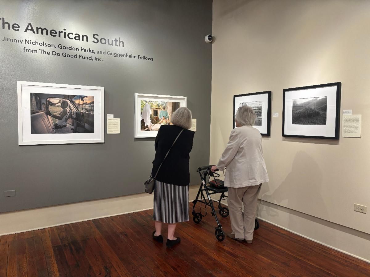 Two visitors viewing framed photographs in a museum gallery with wood floors and gray walls